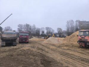Būvlaukums ar kravas automašīnām, smilts un šķembu uzbērumiem, veicot teritorijas sagatavošanas darbus