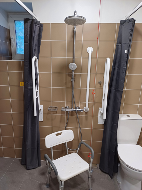 Dušas telpa ar pielāgotu aprīkojumu – rokturiem, dušas krēslu un aizkariem personām ar kustību traucējumiem