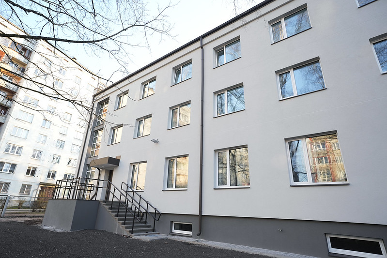 Pašvaldība turpinās uzlabošanas darbus Rīgas Hokeja skolas ēkās -Moderna trīsstāvu daudzdzīvokļu ēka ar gaišu fasādi un vairākām logu rindām; pie ieejas kāpnes, apkārtnē redzama vēl viena līdzīga ēka un kaili koki