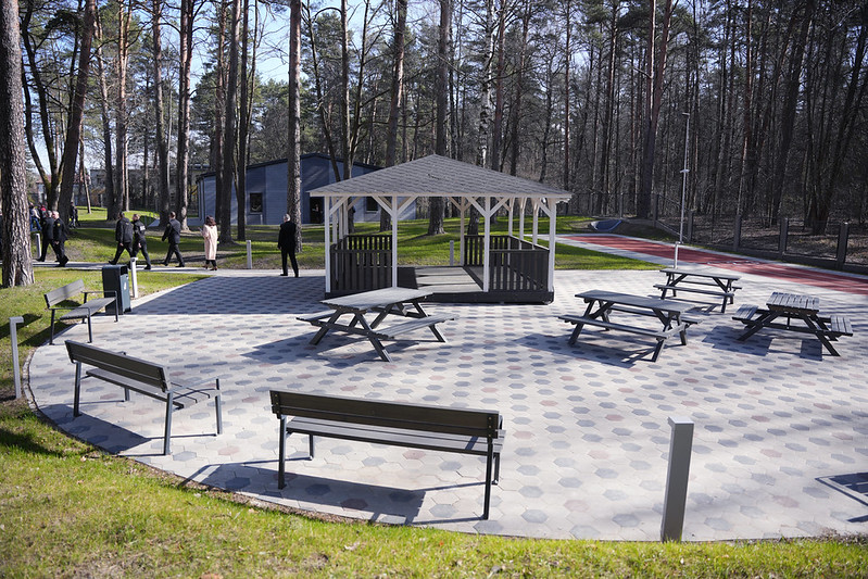 Labiekārtota atpūtas zona ar soliem un galdiem meža teritorijā.