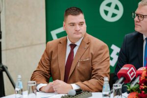 Divi cilvēki sēž pie galda preses konferencē; priekšā mikrofoni ar 'G' un 'LTV' logotipiem