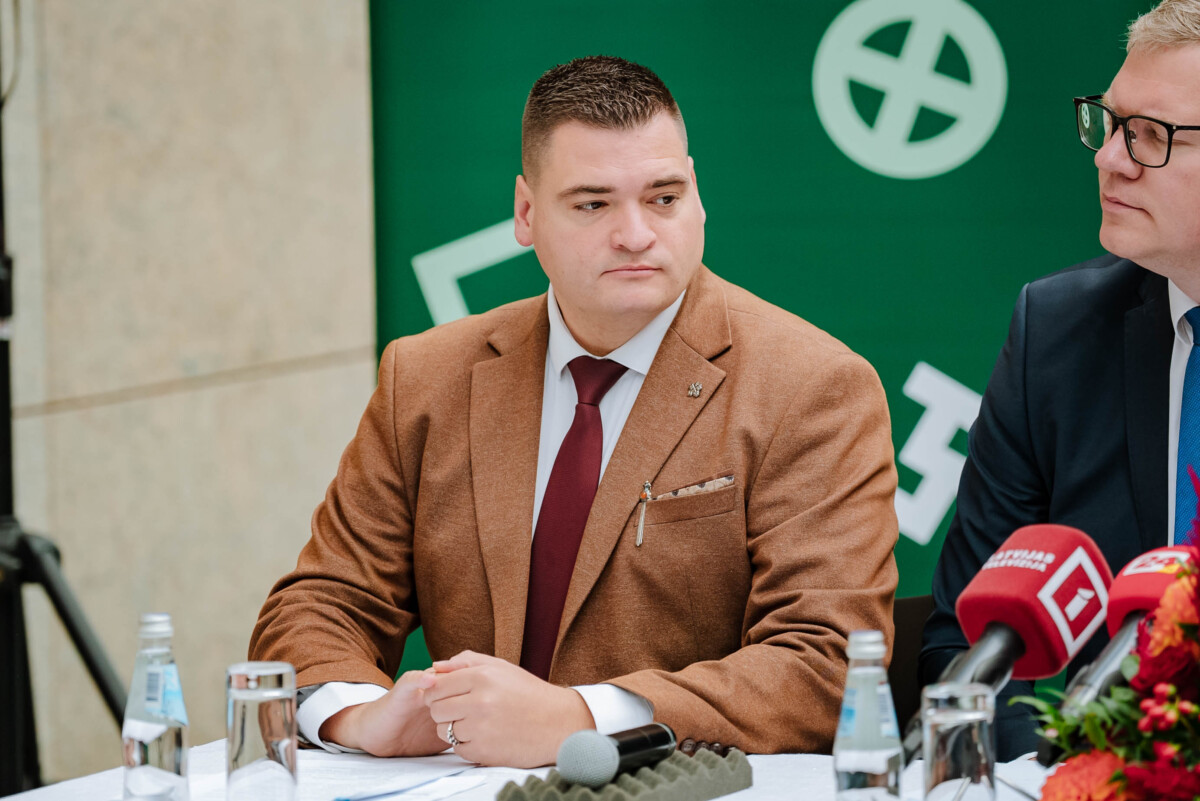 Divi cilvēki sēž pie galda preses konferencē; priekšā mikrofoni ar 'G' un 'LTV' logotipiem