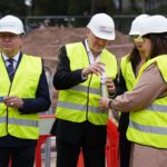 Cilvēku grupa ar aizsargķiverēm un atstarojošām vestēm būvlaukumā