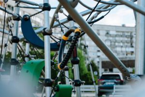 Tuvplāna skats uz rotaļu laukuma kāpšanas konstrukciju ar metāla stieņiem, virvēm un plastmasas elementiem