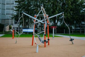 Sporta laukuma dzelzs konstrukcija ar metāla stieņiem, drošs zemes segums, fonā koki, ēka