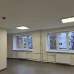 Plaša telpa ar gaišām sienām un tumšu grīdu, divi logi ar baltiem rāmjiem un radiatoriem zem tiem, griestos divi kvadrātveida gaismekļi un sarkans dūmu detektors