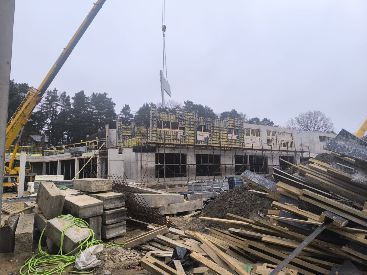 Būvlaukums ar montējamiem dzelzsbetona elementiem, veidņiem un būvmateriāliem ēkas stāvu izbūves procesā