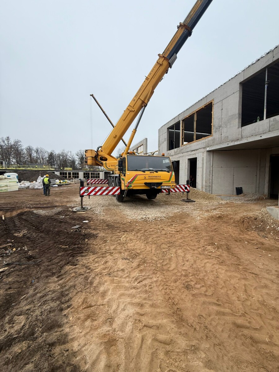 Būvlaukums ar mobilu celtni pie dzelzsbetona ēkas, veicot konstrukciju montāžas darbus