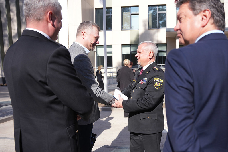 Pasākuma dalībnieki pie ēkas ieejas, notiek oficiāla tikšanās.