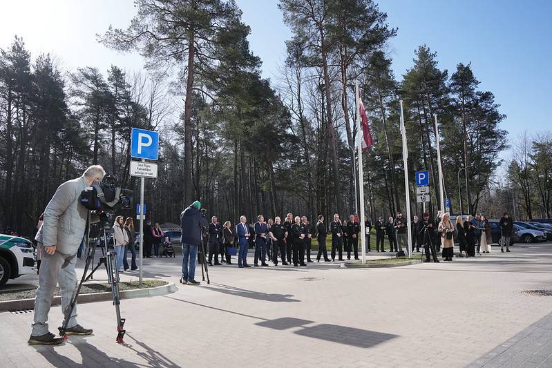 Pasākuma kopskats ēkas priekšā ar dalībniekiem un medijiem.