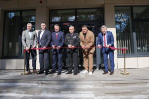 Oficiāls pasākums pie ēkas ieejas ar lentes griešanu.