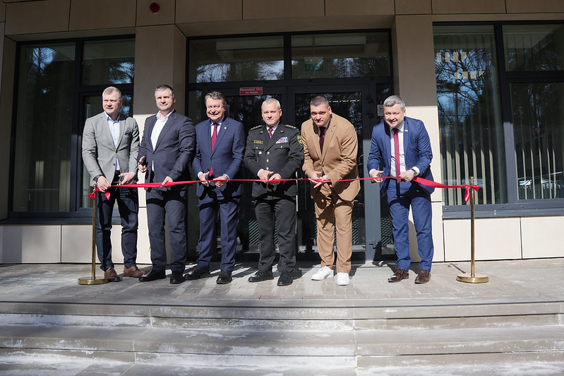 Oficiāls pasākums pie ēkas ieejas ar lentes griešanu.