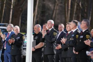 Pasākuma apmeklētāji klausās uzrunu āra teritorijā.