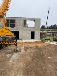 Dzelzsbetona ēkas fasāde būvniecības procesā ar celtni un montāžas darbiem pie logu ailēm