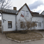 Divstāvu dzīvojamās ēkas foto Čiekurkalna 3. šķērslīnijā 11, Rīgā. Ēkai ir gaiši pelēks fasādes apmetums, slīps jumts un Latvijas karogs pie loga. Priekšā redzams neliels pagalms ar koku un bruģētu celiņu.