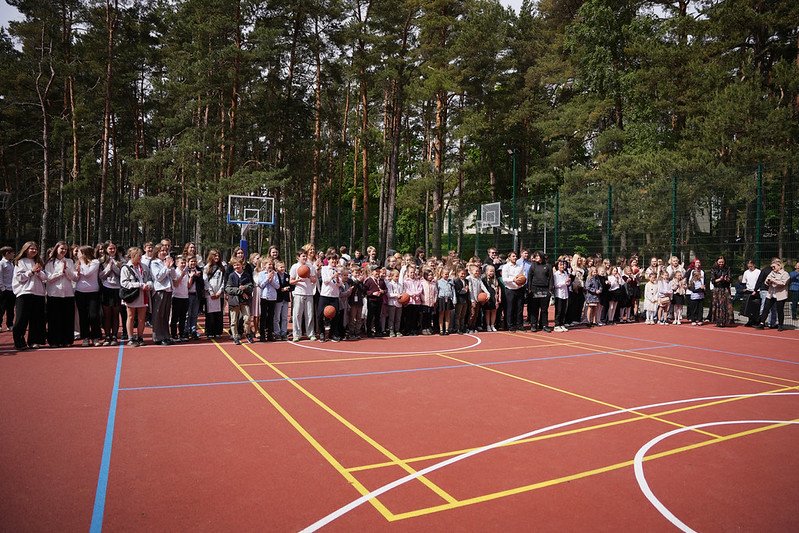Plašs skats uz āra sporta laukumu, kur sapulcējušies skolēni ar basketbola bumbām pasākuma laikā
