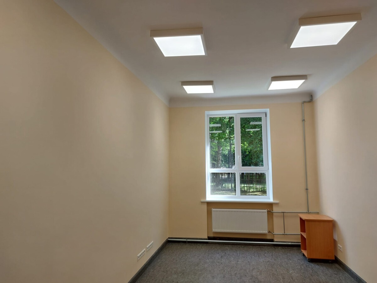 Izremontēta telpa ar logu, radiatoru, griestu apgaismojumu un pieslēgumu vietām pie sienas.