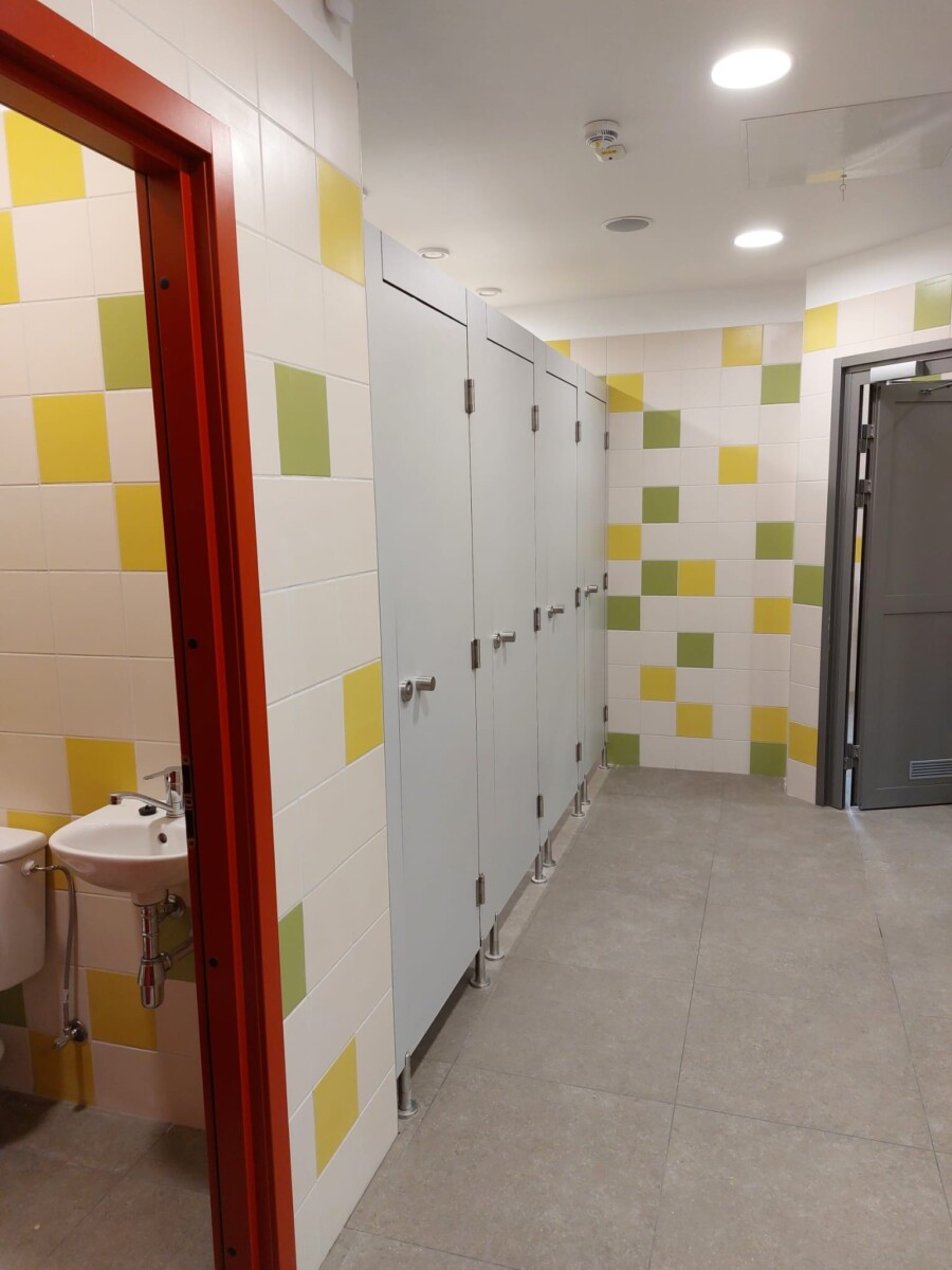 Labiekārtota sanitārā telpa ar tualetes kabīnēm, izlietni un krāsainu flīžu apdari.