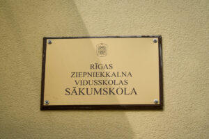 Pie ēkas sienas piestiprināta informatīva plāksne ar uzrakstu “Rīgas Ziepniekkalna vidusskolas sākumskola”